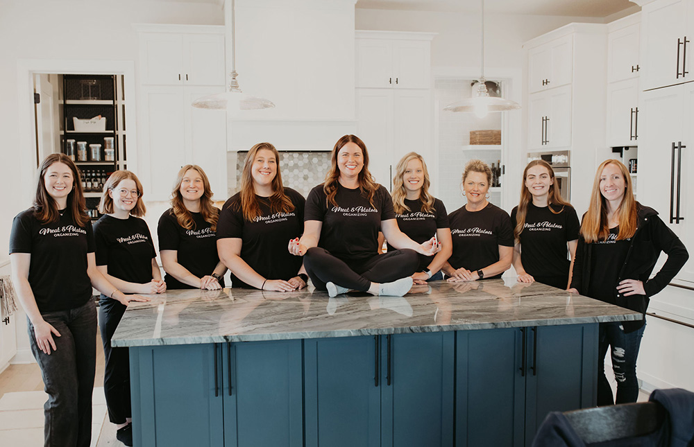 The professional organizing team of Meat and Potatoes Organizing, based in Edina and Prior Lake, standing together in a well-organized room. Experts in organizing, packing, and unpacking services for homes and businesses.